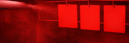 Red powder coating applied to metal parts on hanging hooks in industrial spray booth